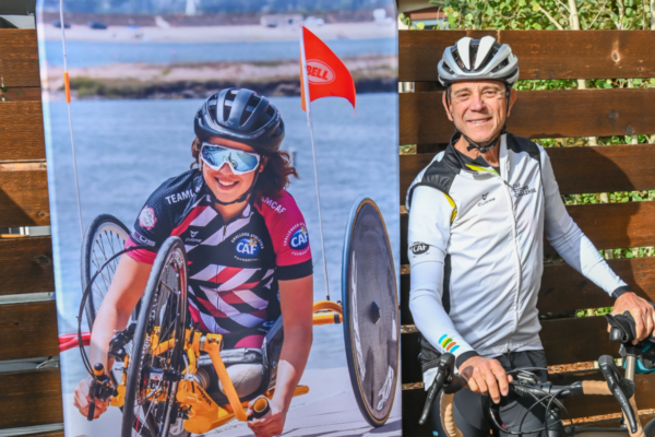 Cyclist stands next to a Challenged Athletes Foundation adaptive handcycling display, highlighting opportunities for athletes with physical disabilities.