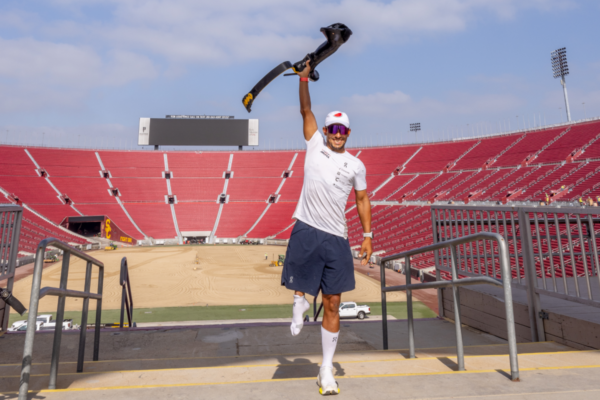 Adaptive athlete raises a running prosthesis at a stadium, symbolizing resilience, innovation, and access to adaptive sports through CAF support.