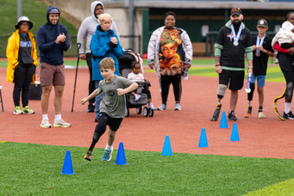 Athletes and supporters participate in a group running exercise during a CAF and Össur adaptive sports clinic on a field in Washington, D.C.