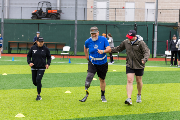 Athlete with a running prosthesis completes a field exercise with guidance from volunteers during a CAF and Össur adaptive sports event.