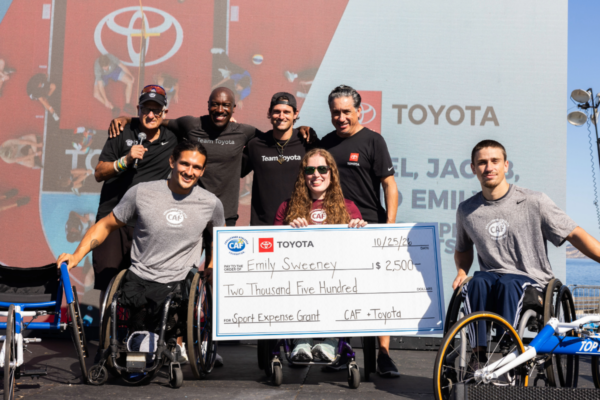 Group of athletes on the main stage of the sandiego traithlon challenge posing for photo with their grants they were awarded