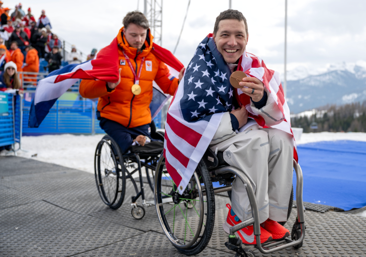Andrew Kurka displays a Paralympic medal while wrapped in an American flag following international adaptive skiing competition.