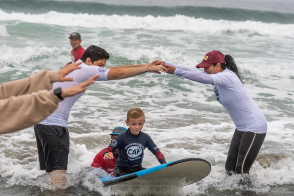 Beauden Baumkirchner participates in adaptive surfing with support from volunteers during a Challenged Athletes Foundation beach program.