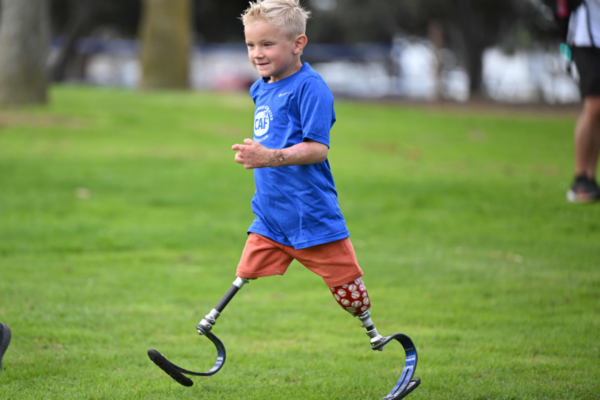 Young adaptive athlete Beauden Baumkirchner runs across a field using running prosthetics during a Challenged Athletes Foundation sports event.