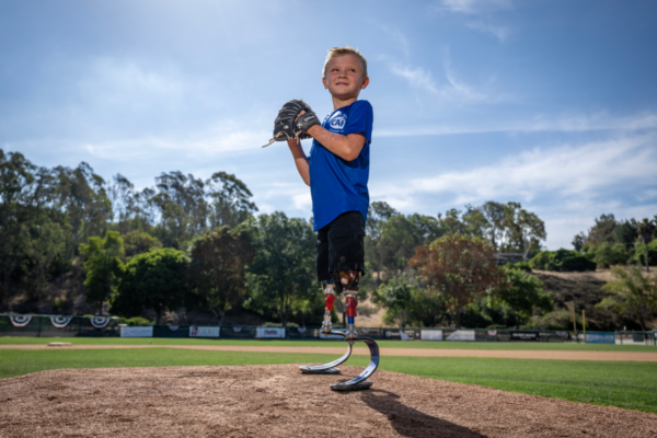 Beauden Baumkirchner stands on a baseball pitcher's mound with a glove, demonstrating his passion for sport and active living.