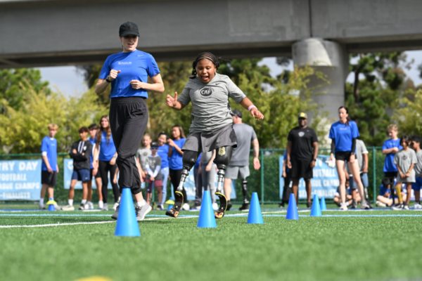 Young athlete with bilateral running prosthetics navigates an agility drill during a CAF and Össur adaptive sports clinic.
